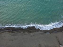 antenne visie van donker strand met klein golven spatten foto