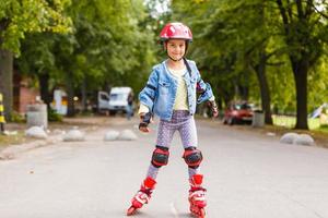 grappig weinig mooi meisje Aan rol skates in helm rijden in een park. gezond levensstijl concept. foto