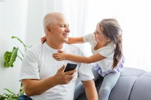 weinig meisje met haar opa gebruik makend van smartphone Bij huis, ruimte voor tekst. familie tijd foto