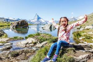 schattig weinig meisje buitenshuis in de gazon en bewonderend bergen visie in berg in Zwitserland foto