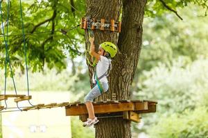 weinig meisje is staand Aan een touw, Holding een touw met zijn handen. een kind in een touw park passeert obstakels foto