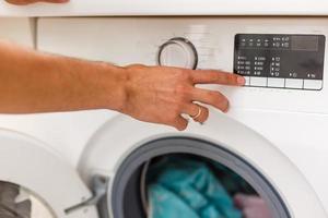 Mens bezig met laden doeken naar het wassen machine. visie van binnen de het wassen machine. foto