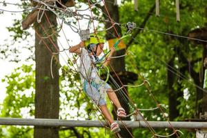 aanbiddelijk weinig meisje genieten van haar tijd in beklimming avontuur park Aan warm en zonnig zomer dag. zomer activiteiten voor jong kinderen. kind hebben pret Aan school- vakanties. foto