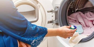 een dichtbij omhoog van een jong vrouw zetten een kleding in het wassen machine foto