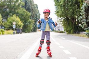 grappig weinig mooi meisje Aan rol skates in helm rijden in een park. gezond levensstijl concept. foto