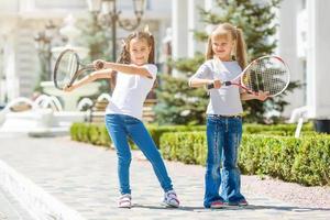 gelukkig preteen meisjes in sport outfits met tennis rackets Aan groen gras achtergrond foto