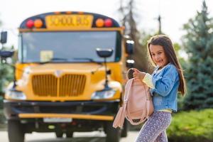 weinig meisje met rugzak gaat naar school- bus foto