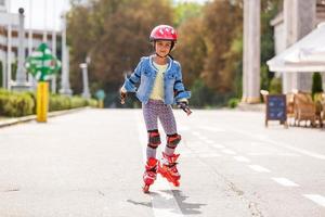 grappig weinig mooi meisje Aan rol skates in helm rijden in een park. gezond levensstijl concept. foto