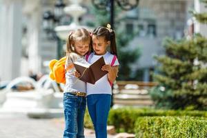 twee school- meisjes vervelend rugzak buiten de primair school. schoolmeisje, elementair school- leerling gaan van school, diploma uitreiking, zomer vakantie. foto