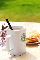 Washington, Verenigde Staten van Amerika - augustus 01 2022 koffie mok met Starbucks logo Aan voorkant, wit bakkerij Aan bord. plaats het Aan een houten tafel in de tuin waar de ochtend- zon schijnt. foto