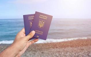 twee biometrisch oekraïens paspoorten in hand- Aan zee kust achtergrond foto