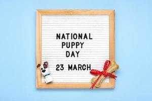 voelde bord met tekst nationaal puppy dag in 23 maart, schattig hond figuren, kauwen bot met boog Aan blauw achtergrond top visie vlak leggen vakantie groet kaart foto
