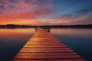 kleurrijk houten pier Aan een meer dat is totaal kalmte gedurende zonsondergang foto