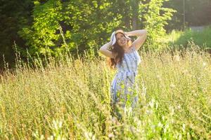 gelukkig jong vrouw met lang haar- in hoed en jurk wandelen door de zomer Woud Aan een zonnig dag. zomer vreugde concept foto