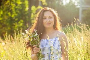 jong vrouw wandelen tussen wilde bloemen Aan zonnig zomer dag. concept van de vreugde van communiceren met zomer natuur foto