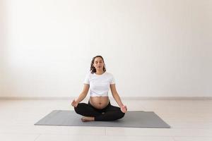 gezond mooi zwanger vrouw mediteert voordat yoga klasse en ontspant terwijl zittend Aan mat Aan de vloer. concept van fysiek en mentaal voorbereiding van lichaam voor bevalling. copyspace foto