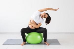 een jong zwanger vrouw aan het doen oefening gebruik makend van een geschiktheid bal terwijl zittend Aan een mat. foto