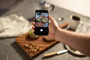 handen nemen afbeeldingen Aan smartphone van twee mooi gezond verzuren room en avocado boterhammen aan het liegen Aan bord Aan de tafel. sociaal media en voedsel concept foto