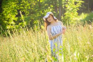 gelukkig jong vrouw met lang haar- in hoed en jurk wandelen door de zomer Woud Aan een zonnig dag. zomer vreugde concept foto