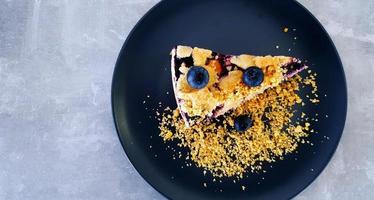 top visie van bosbes crumble Aan zwart schotel of bord Aan grijs beton achtergrond met kopiëren ruimte Aan links. vlak leggen van toetje Aan grijs tafel Bij caf winkel. voedsel handgemaakt met fruit en prima crackers. foto