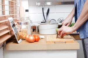 Aziatisch mannen zijn gelukkig naar koken in de keuken Bij huis. aan het kijken videos online aan het leren door tablet. voedsel concept. foto