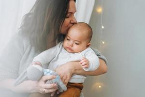 jong moeder spelen met schattig baby jongen in helder slaapkamer, natuurlijk tonen, liefde emotie foto