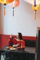 mooi jong Aziatisch vrouw in rood kleren aan het eten Aziatisch voedsel in feestelijk Chinese Vietnamees restaurant kleurrijk papier lantaarns vieren Chinese nieuw jaar foto