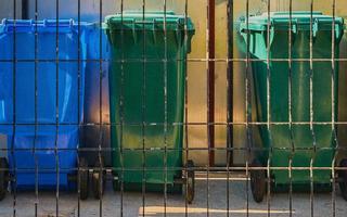 vuilnis veelkleurig buitenshuis plastic bakken achter een metaal rooster, buitenshuis bakken voor scheiden verspilling van gerecycled materialen. foto