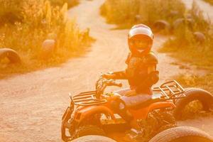 de weinig meisje ritten een quad fiets atv. een mini quad fiets is een koel meisje in een helm en beschermend kleding. elektrisch quad fiets elektrisch auto voor kinderen populariseert groen technologie. foto