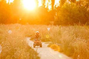 gelukkig weinig meisje spelen Aan weg Bij de dag tijd. hij het rijden Aan quad fiets in de park. kind hebben pret Aan de natuur. concept van geluk. foto