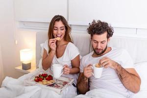 jong getrouwd paar in liefde aan het eten ontbijt in hun bed. mooi zo ochtend- gezond ontbijt in bed. jong mooi liefde paar is hebben ontbijt in bed. foto