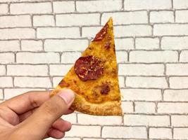 hand- gehouden pizza plak tegen wit steen muur achtergrond foto