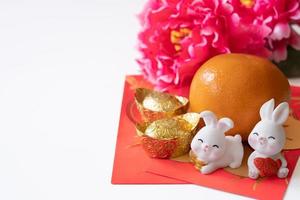 Chinese nieuw jaar van de konijn festival concept. oranje, rood enveloppen, twee konijnen en goud baar versierd met Pruim bloesem Aan wit achtergrond. foto