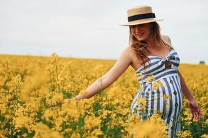 zwanger vrouw poseren Aan een veld- van geel bloemen foto