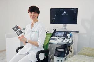 portret van verloskundige dokter dat zit in de kliniek kamer met echografie apparaat foto