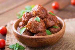 gehaktballen in zoet en verzuren tomaat saus en basilicum in een houten kom foto