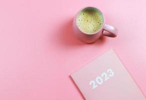 vlak leggen van roze 2023 dagboek of ontwerper met roze kop van koffie Aan roze achtergrond. nieuw jaar plannen of resoluties concept. foto