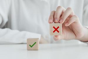 menselijk plukken mis of rood kruis icoon Aan hout kubus van groen controleren Mark voor waar of false manier van denken of verkiezingen stemmen, enquête en beoordeling naar verandering leider en transformeren quiz antwoord en poll concept. foto