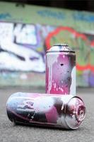 een weinig gebruikt verstuiven blikjes met roze en wit verf liggen Aan de asfalt tegen de achtergrond van een geschilderd muur in kleurrijk graffiti tekeningen foto