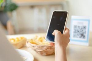 vrouw gebruik smartphone naar scannen qr code in cafe. de restaurant gebouwd een digitaal betaling systeem zonder contant geld. qr code betalen, e portemonnee, contant geld technologie, betalen online foto