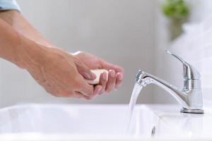 mannen het wassen handen met zeep en schoon water in voorkant van de badkamer wastafel naar voorkomen de verspreiding van bacterieën. het wassen handen met zeep. foto