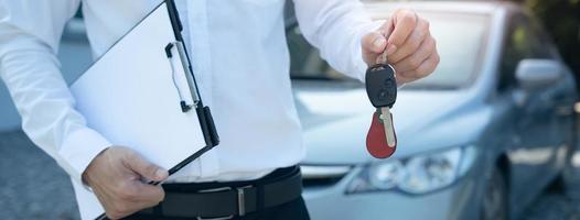 verkoop auto, auto uitverkoop, transactie concept de handelaar geeft de auto sleutels naar de nieuw eigenaar of huurder met een verzekering contract. foto