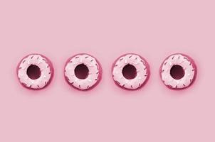 veel klein plastic donuts leugens Aan een achtergrond. vlak leggen minimaal patroon. top visie beeld afgezwakt in viva magenta, kleur van de 2023 jaar foto