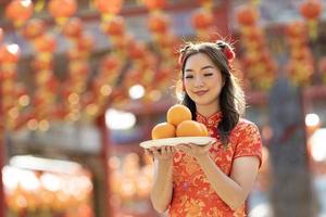 Aziatisch vrouw in rood cheongsam qipao jurk is aanbieden mandarijn naar de voorouderlijk god binnen Chinese boeddhistisch tempel gedurende maan- nieuw jaar voor het beste wens zegen en mooi zo geluk concept foto