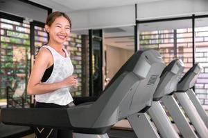 jong gelukkig Aziatisch vrouw atleet rennen Aan loopband, rennen machine, in binnen- Sportschool geschiktheid voor Gezondheid foto