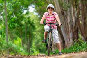 senior bedrijf vrouw, vrouw, rijden of fiets berg fiets in land park in de buurt huis stad- voor gezond oefening in zomer weekend foto