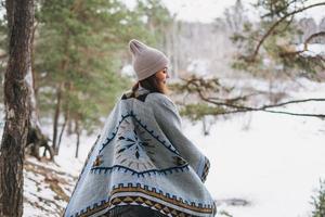 jong brunette mooi vrouw in hoed en grijs poncho wandelen in de winter Woud foto