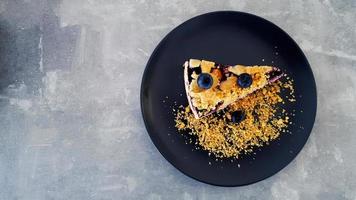 top visie van bosbes crumble Aan zwart schotel of bord Aan grijs beton achtergrond met kopiëren ruimte Aan links. vlak leggen van toetje Aan grijs tafel Bij caf winkel. voedsel handgemaakt met fruit en prima crackers. foto