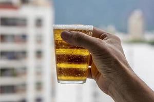 Mens Holding glas van bier Aan wazig stedelijk stad achtergrond foto