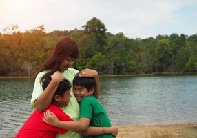 gelukkig familie uitgeven tijd buitenshuis knuffelen en genieten van de visie van rivier. moeder met twee kinderen. foto